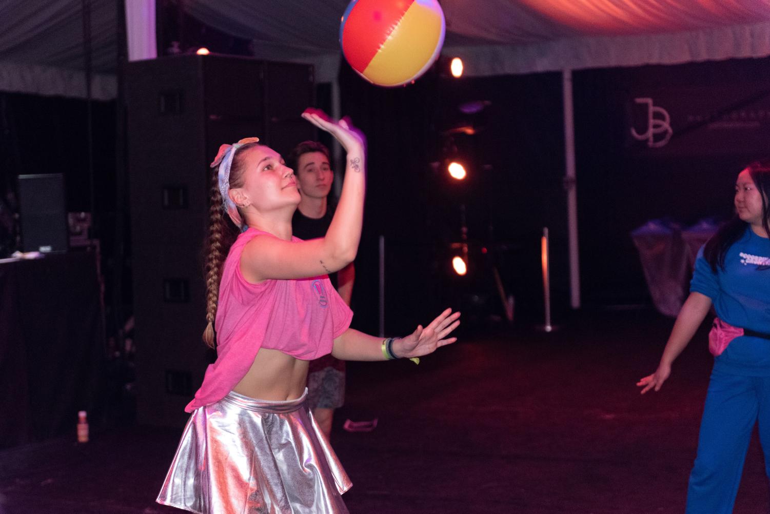 A person in a pink crop top hits a colorful beach ball with one hand. 