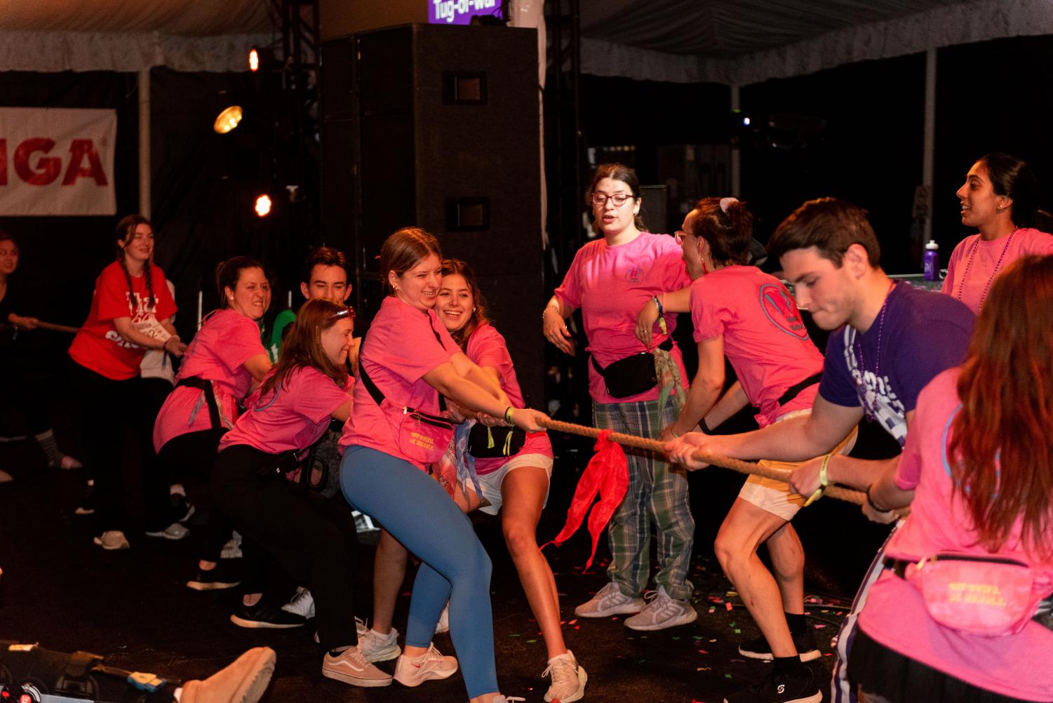 A group of people in pink shirts pull a rope in a game of tug of war. 
