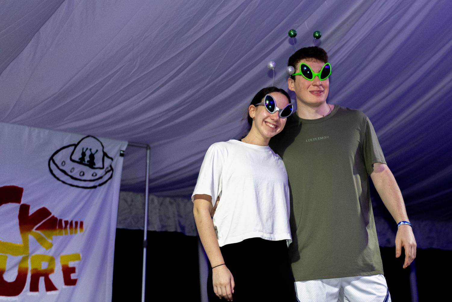 Two people in alien glasses stand with arms around each other. 