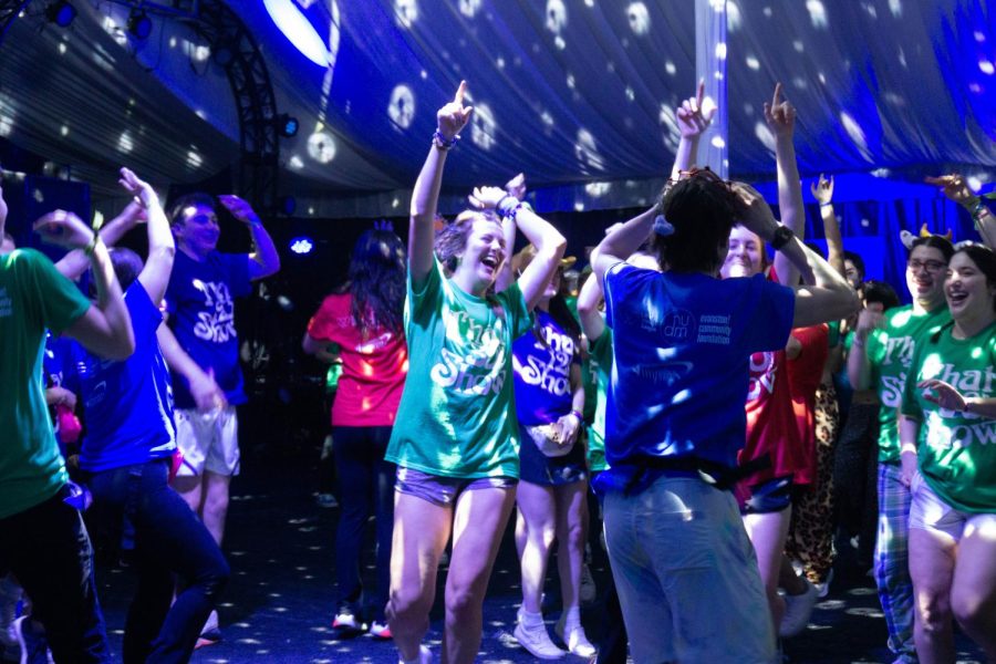 People wearing blue shirts, green shirts and red shirts dance.