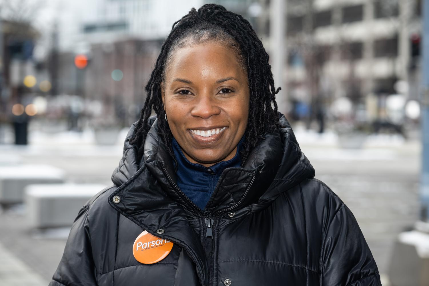 A+woman+wearing+a+black+puffy+coat+and+an+orange+pin+that+says+Parsons+looks+at+the+camera.