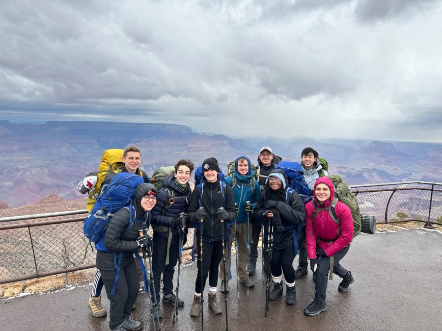 The+experienced+group+posing+for+a+photo+on+top+of+the+Grand+Canyon+holding+hiking+poles+and+gear+with+gray+cloudy+skies+in+the+background.