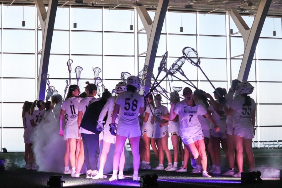 Players wearing white jerseys stand in a group and hold their sticks together in the air with smoke and purple lighting.