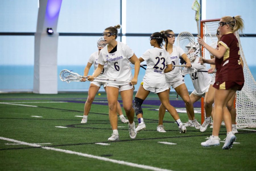 An athlete in a white jersey holds a lacrosse stick in front of her.