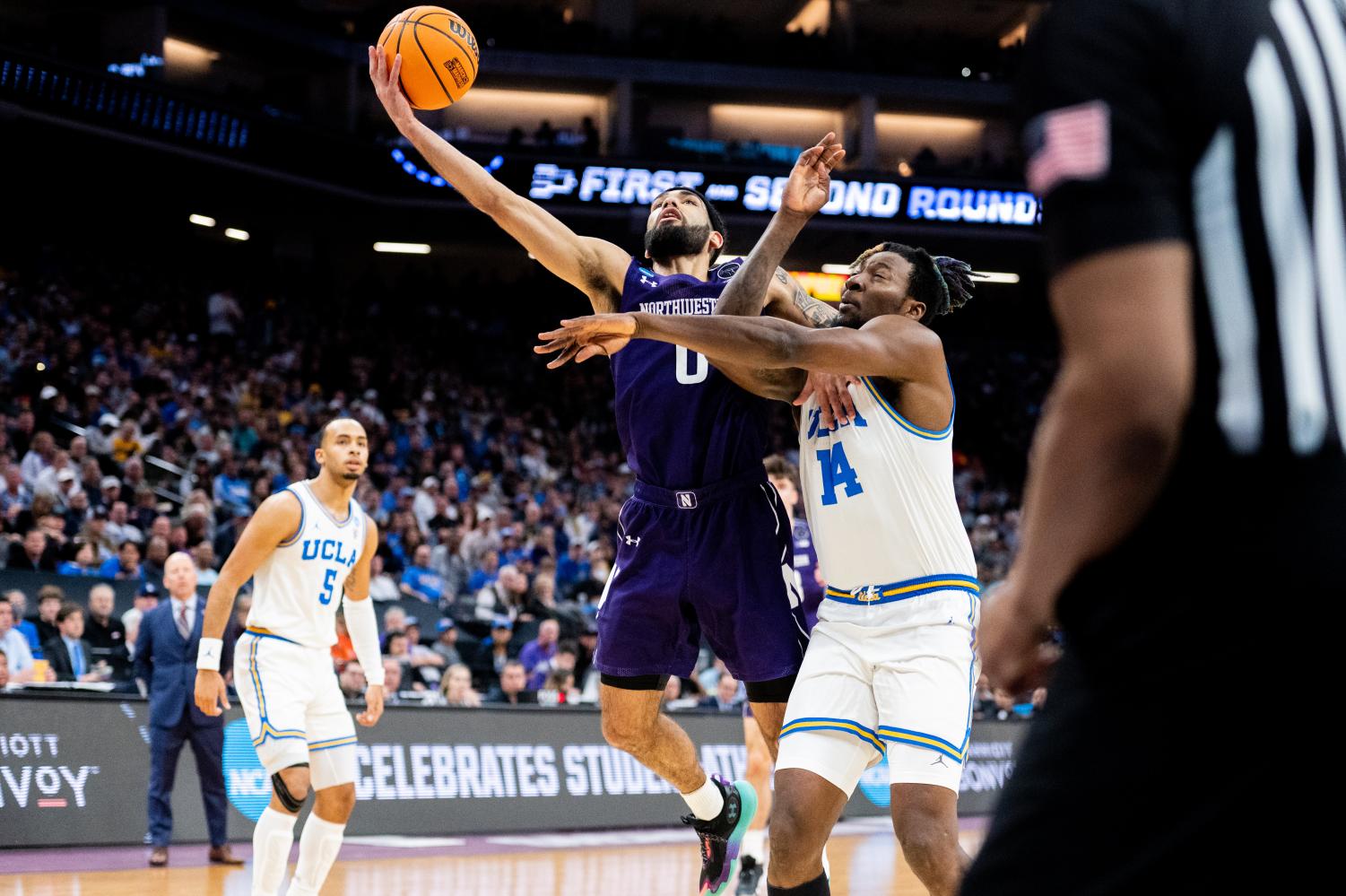 A player in purple jumps up to catch a basketball while pushing another player in white away.