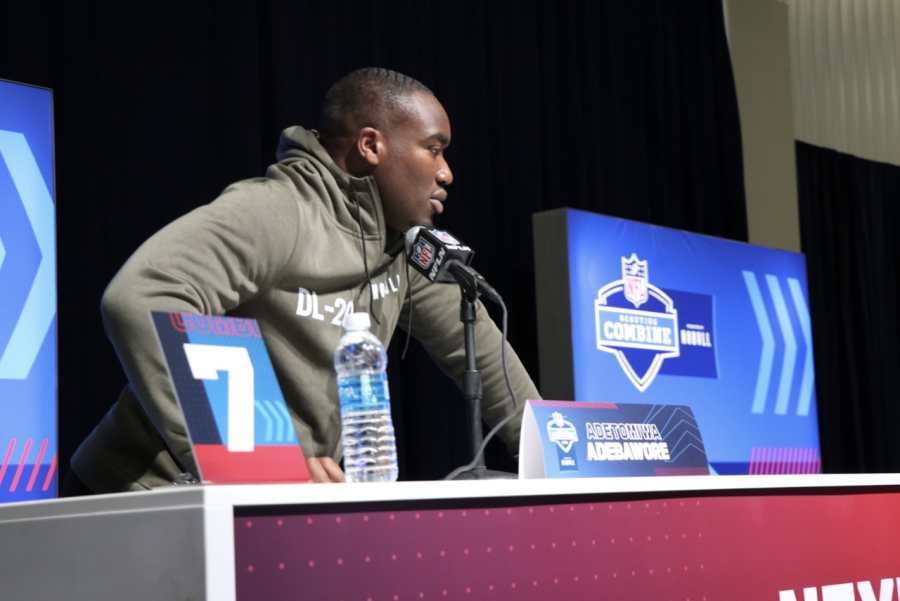 A football player in gray hoodie talks into a microphone.