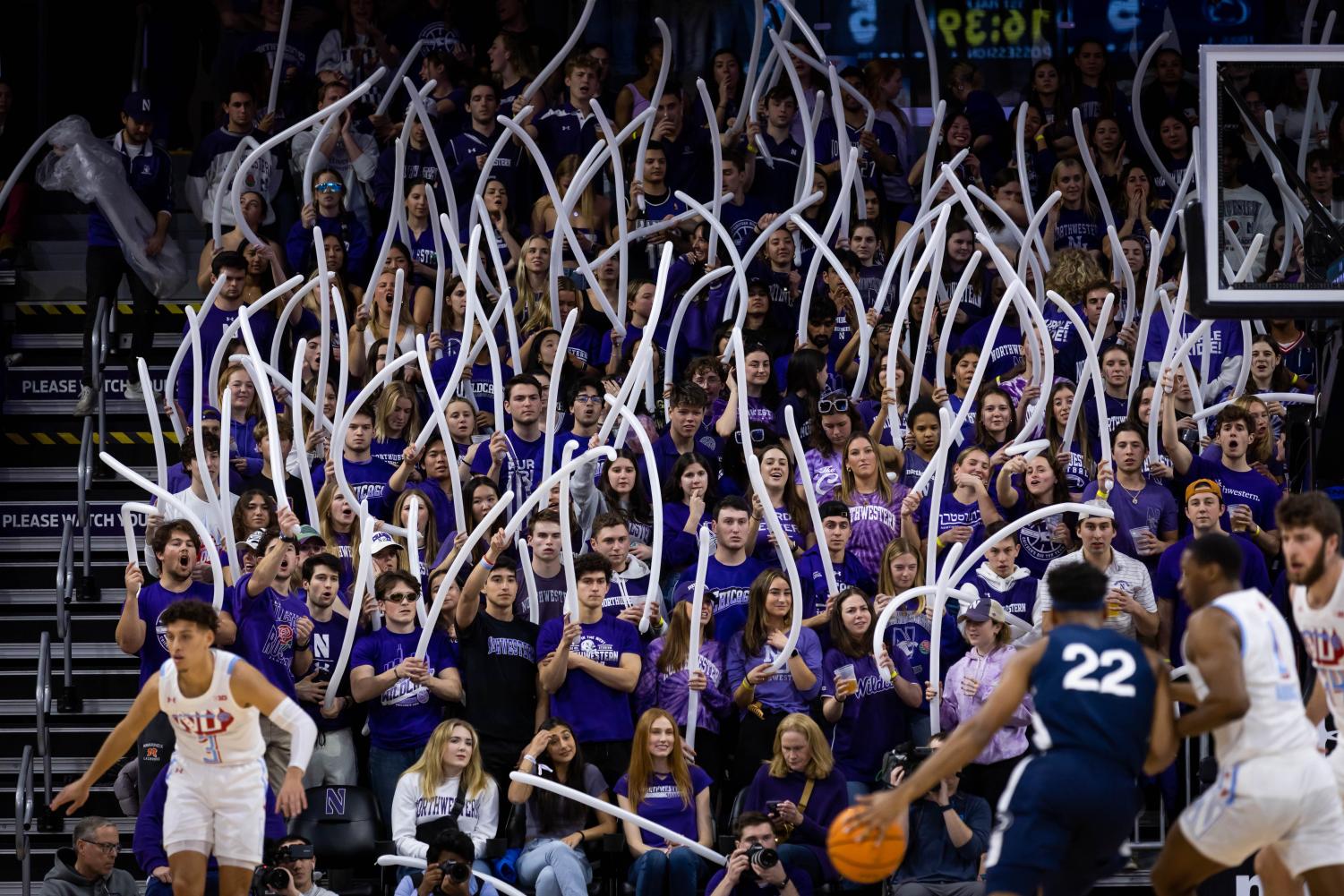 A crowd wearing purple shakes long white balloons in the air.