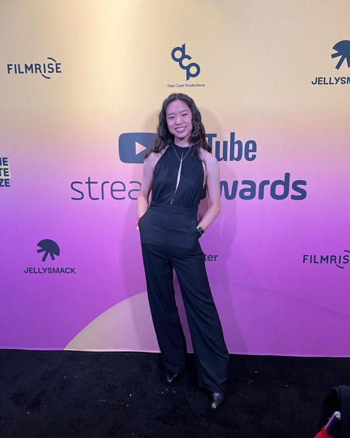 Ashley stands on a black carpet in front of a banner.