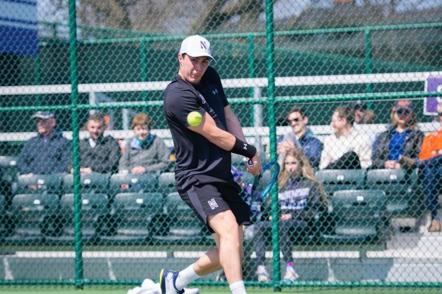 A man wearing a black shirt and black shorts holds back his tennis racket as the yellow tennis ball comes.