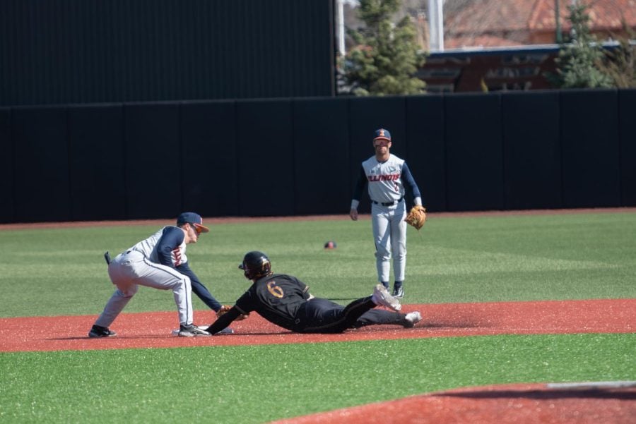 A baseball player in a black uniform slides into second base.