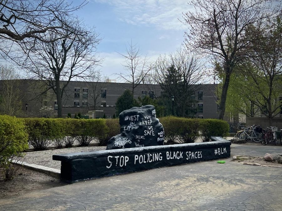 Photograph of a large boulder painted black with Stop policing Black spaces and other phrases in white lettering.