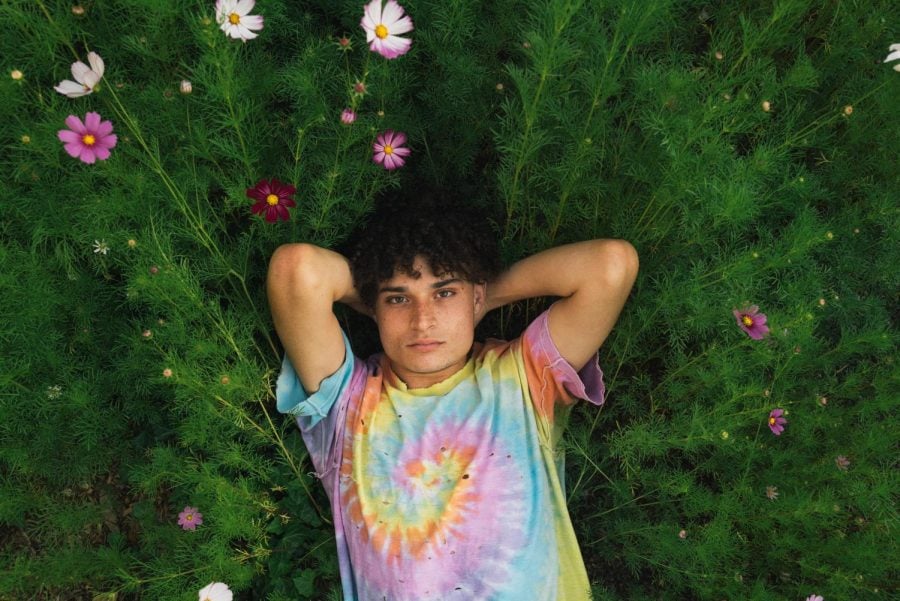 A person in a tie-dye shirt lies in a field of green grass and flowers.