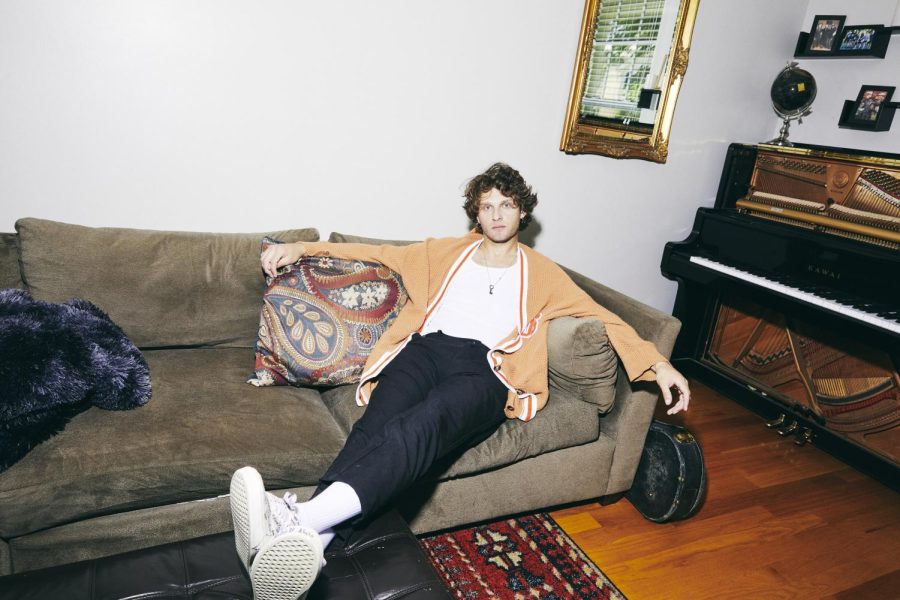 A man in an orange sweater lounges on a couch.