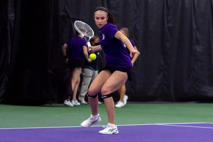 Player in purple shirt takes swing with a tennis racket.