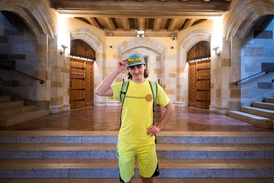 A man in a bright neon-yellow shirt and shorts poses in front of a brown staircase.