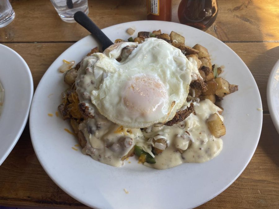 The Chicken Fried Chicken Skillet sits on a white plate on top of a wooden table.
