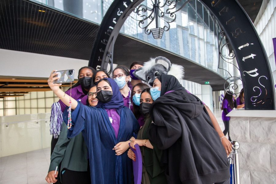 A group of students gather together, with one student holding out a phone to take a photo. Behind them is an arch with the words “Northwestern University.”