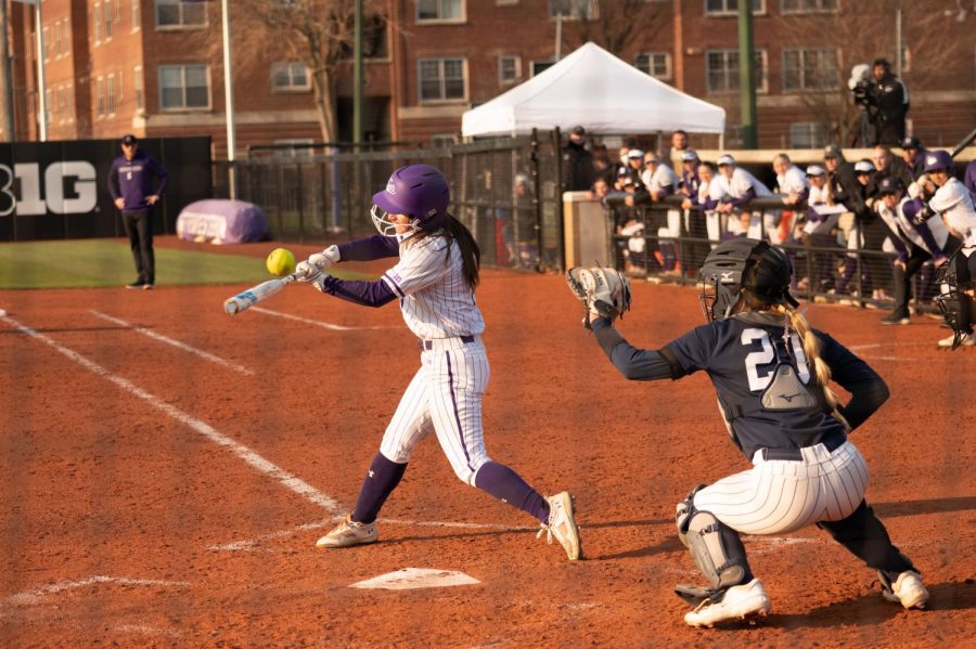 A softball player in a white jersey swings a bat.