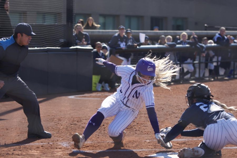 Softball player in purple and white striped uniform runs to home plate.