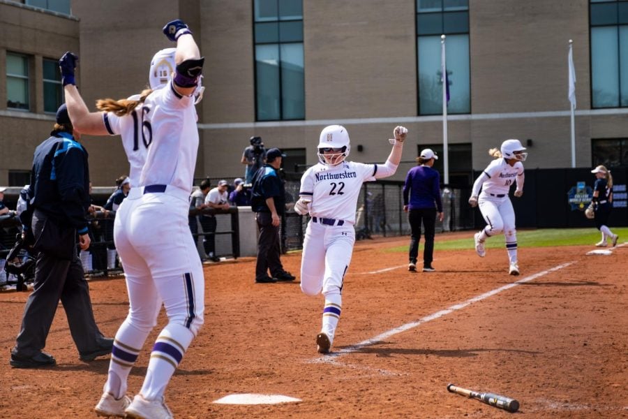 Softball players in purple and white uniforms cheer as one runs to home plate.