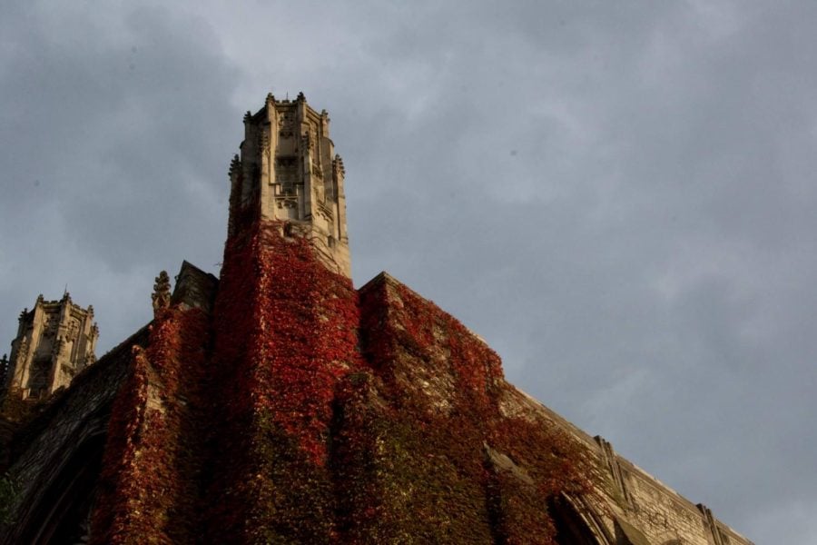A tower of a building covered in red ivy juts into a gray sky.