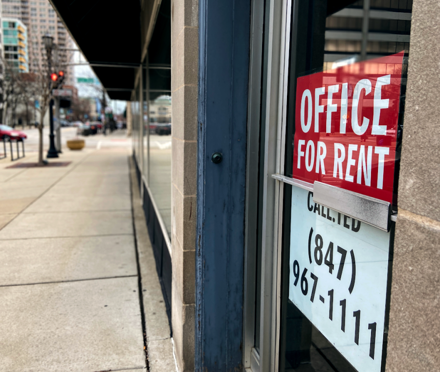 A red “Office for Rent” sign sits on a vacant storefront behind a sidewalk.