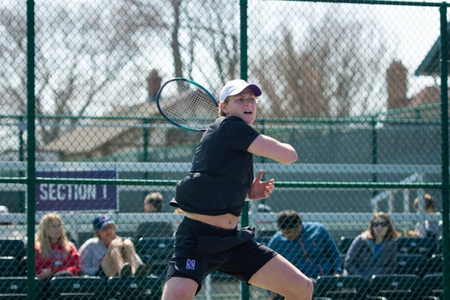 A man in a black shirt and black shorts swings a tennis racket.