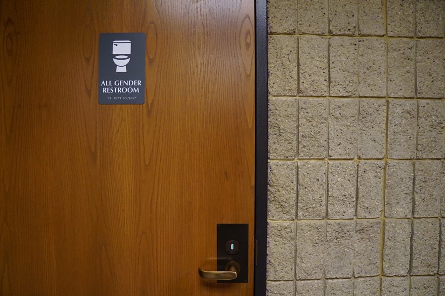 A brown door has a sign on it that reads “all-gender restroom.”