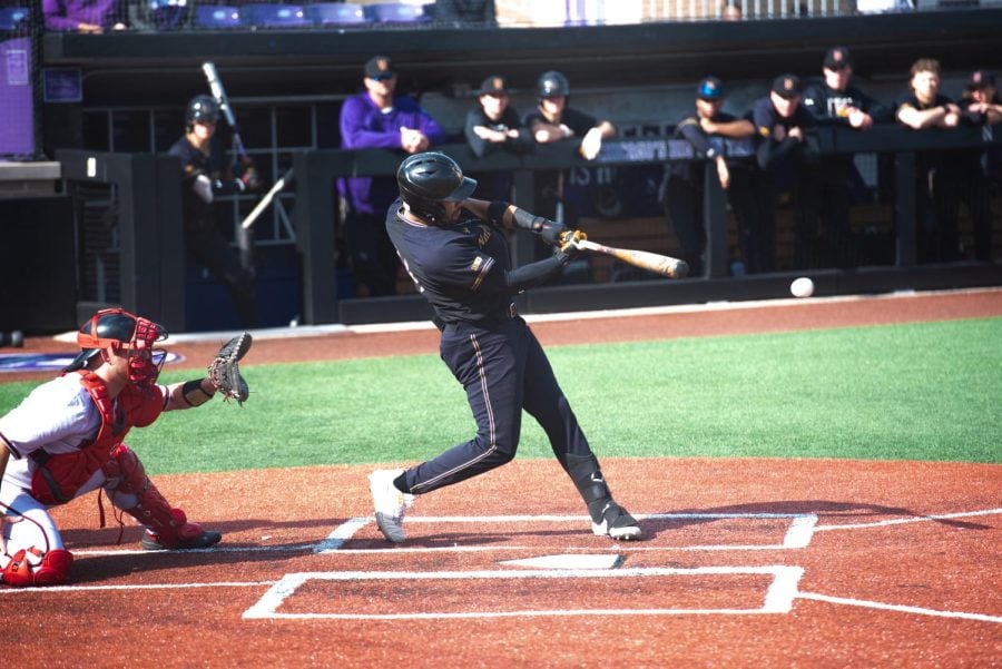 A baseball player in a black uniform swings the bat.