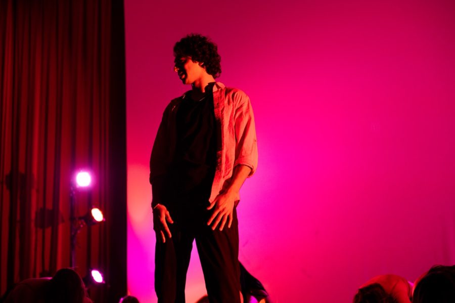 A dancer wearing a flannel on top of dark clothes looks off to the left.
