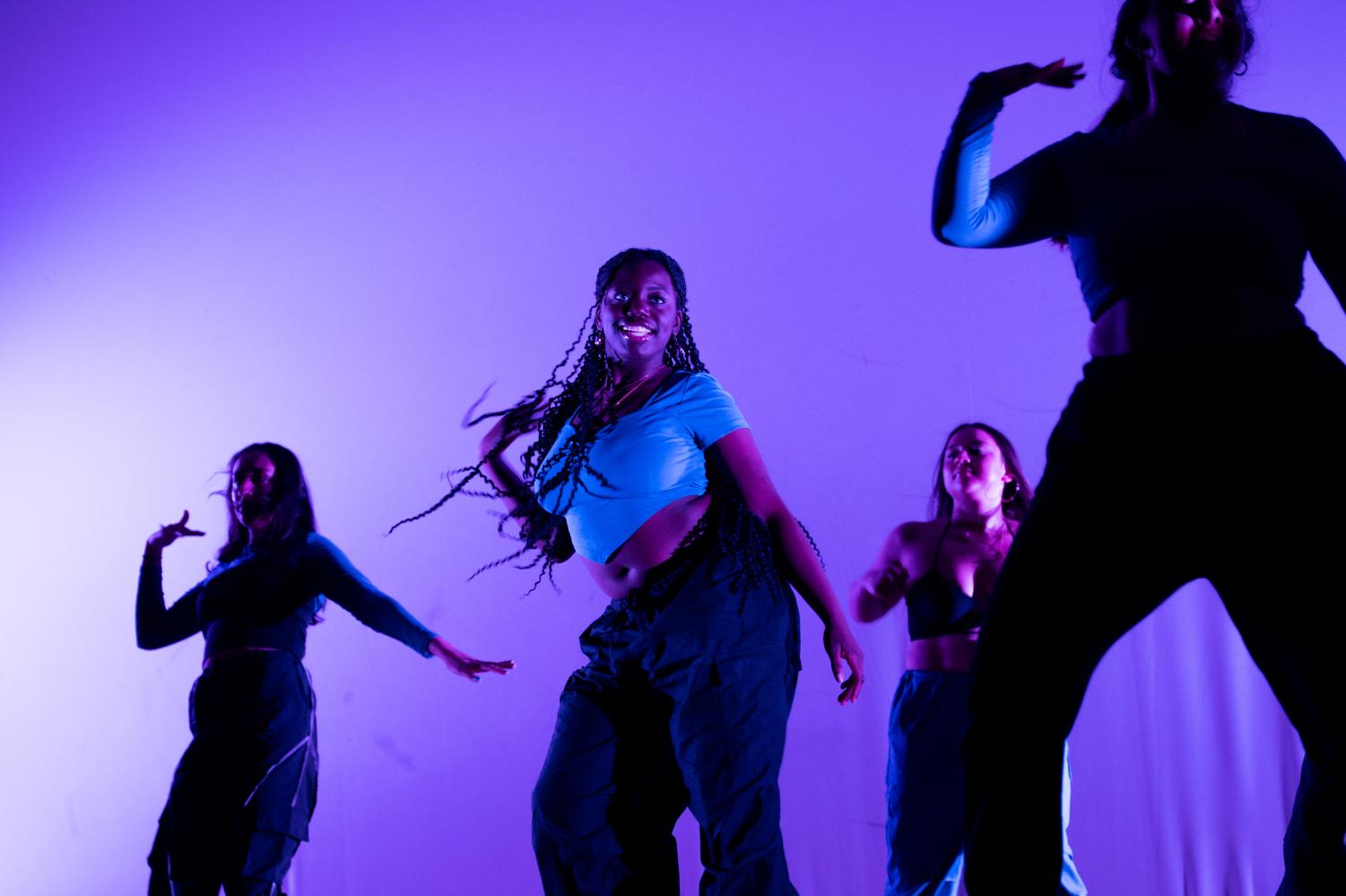 A dancer in the middle of a formation wearing a blue top and black pants smiles. 