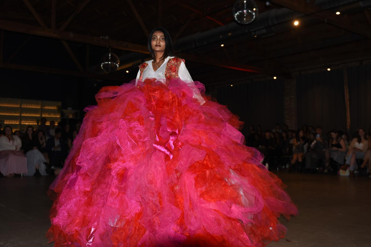 A model wearing a bright pink and red gown walks down a runway.