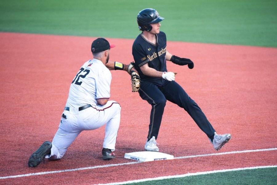 A baseball player in a black uniform runs back to first base.
