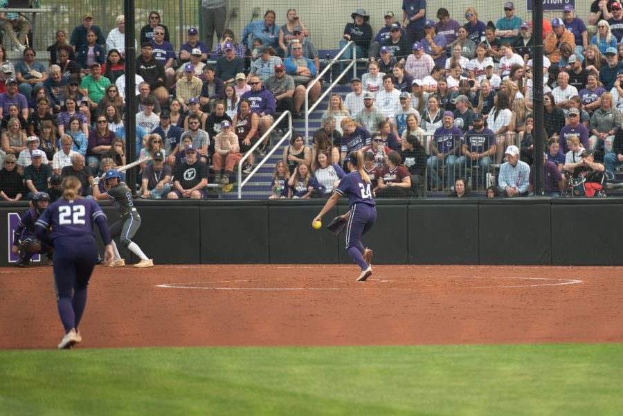 Softball player in purple-and-white uniform pitches the ball.