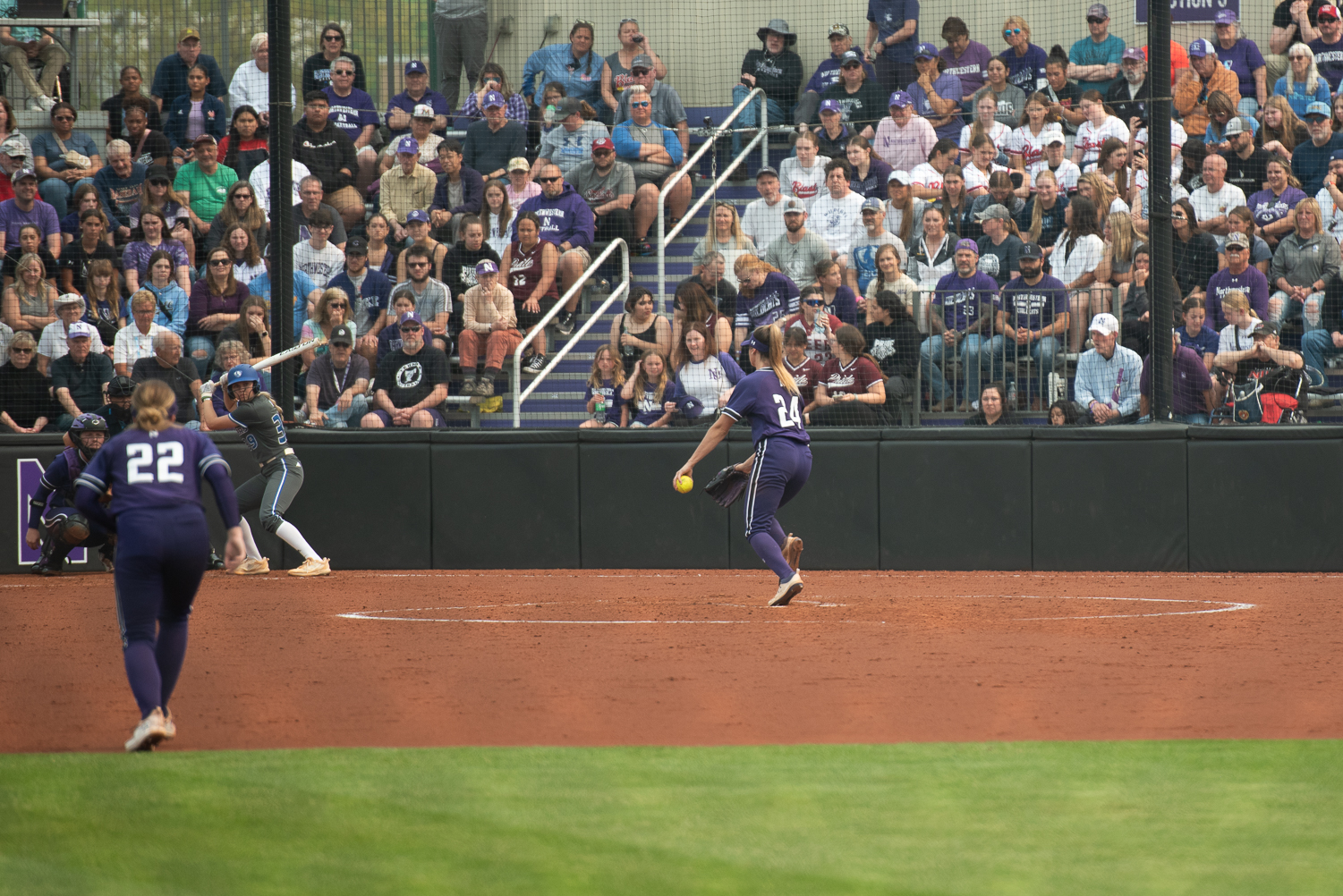 Softball+player+in+purple-and-white+uniform+pitches+the+ball.