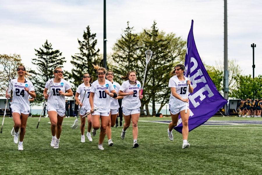 Seven athletes in white jerseys run as one carries a purple flag.