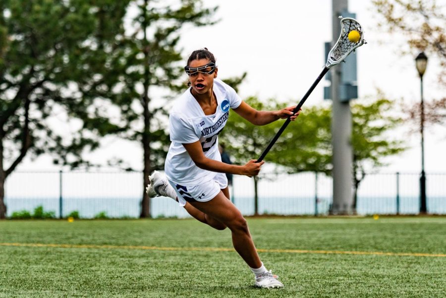 An athlete in a white jersey cradles a lacrosse ball