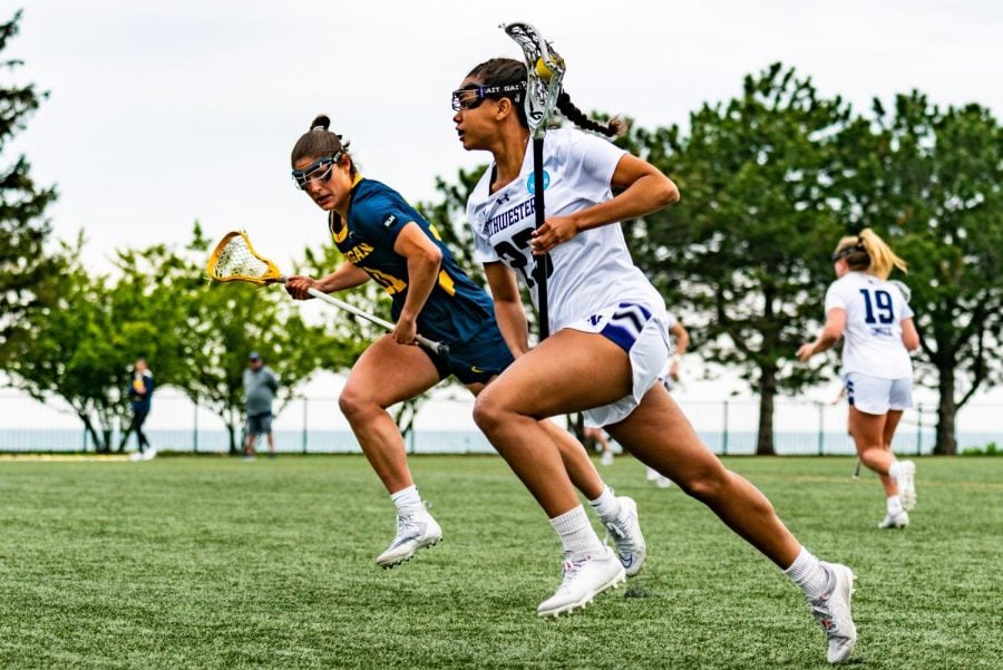 A lacrosse player cradles the ball in her stick and runs down the field.