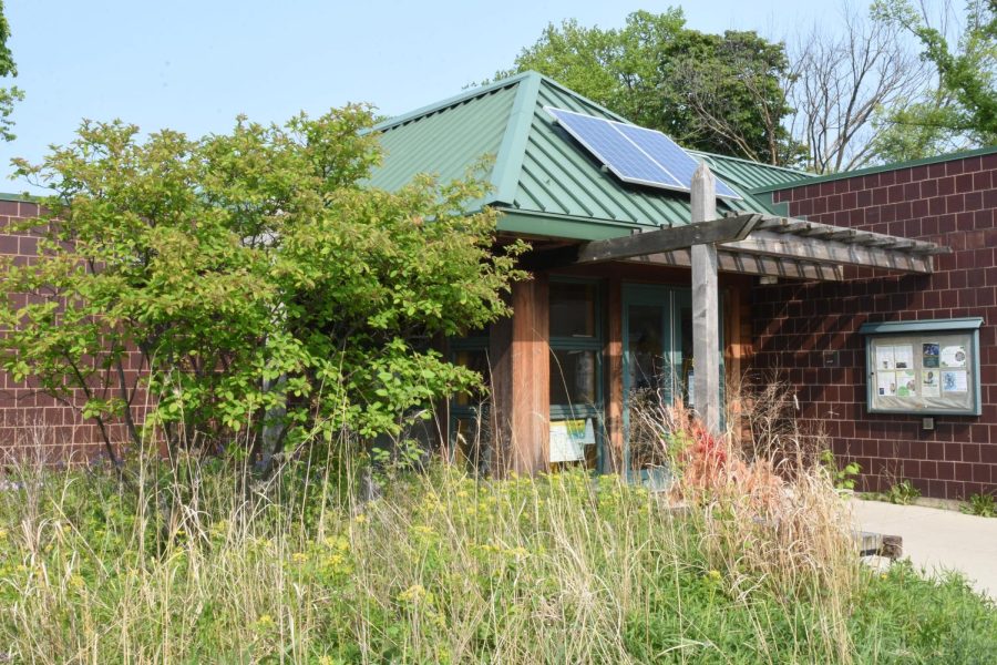 A brick building with a green roof is surrounded by brush.