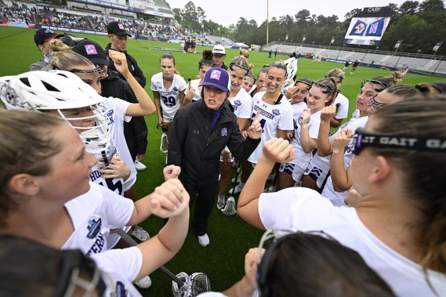 A coach in a black hat talks to her players in white jerseys.