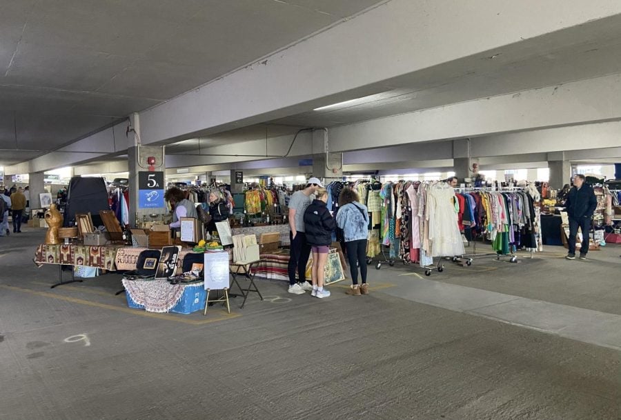 People browse through clothing racks and tables in a gray parking garage.