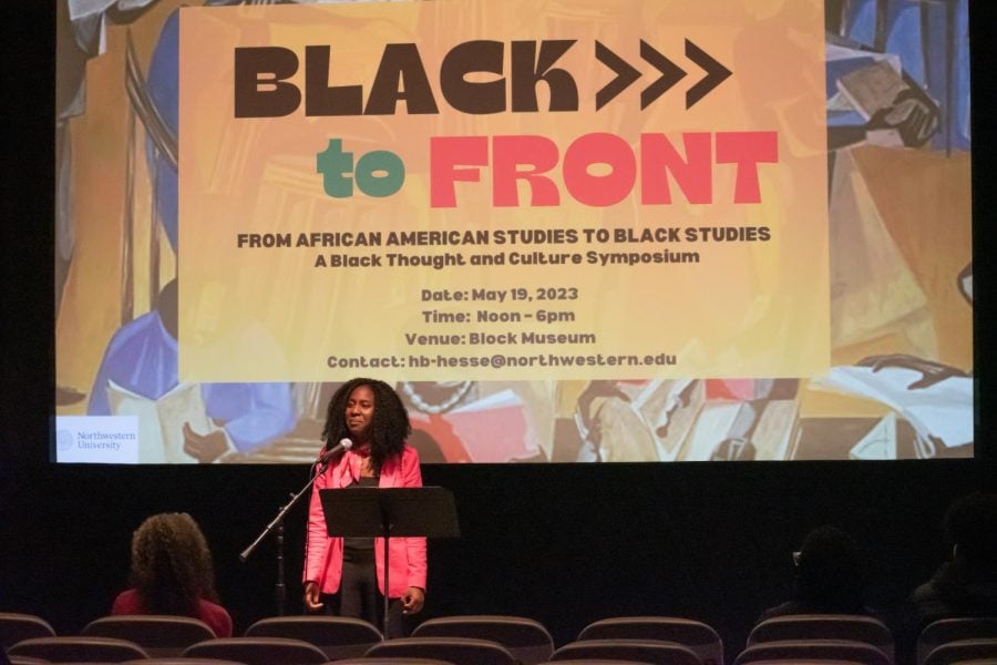 Cydney Hope Brown wears pink clothing with “Black to Front” symposium graphic behind her.