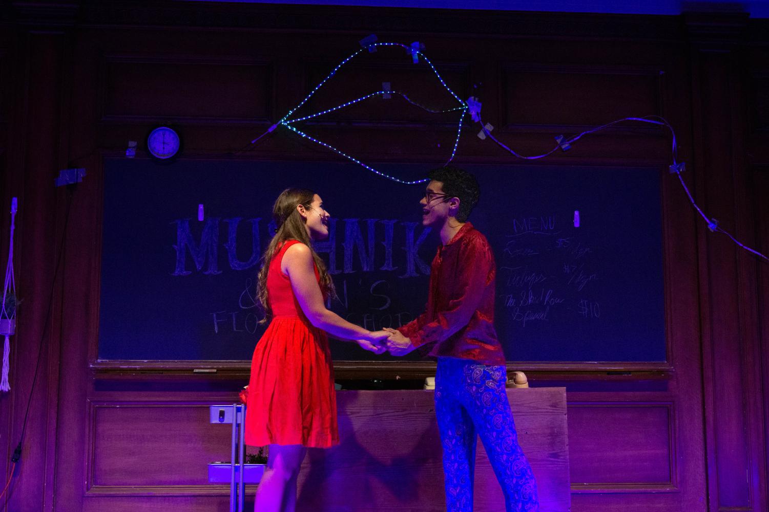 Two performers in red clothes hold hands center of stage.