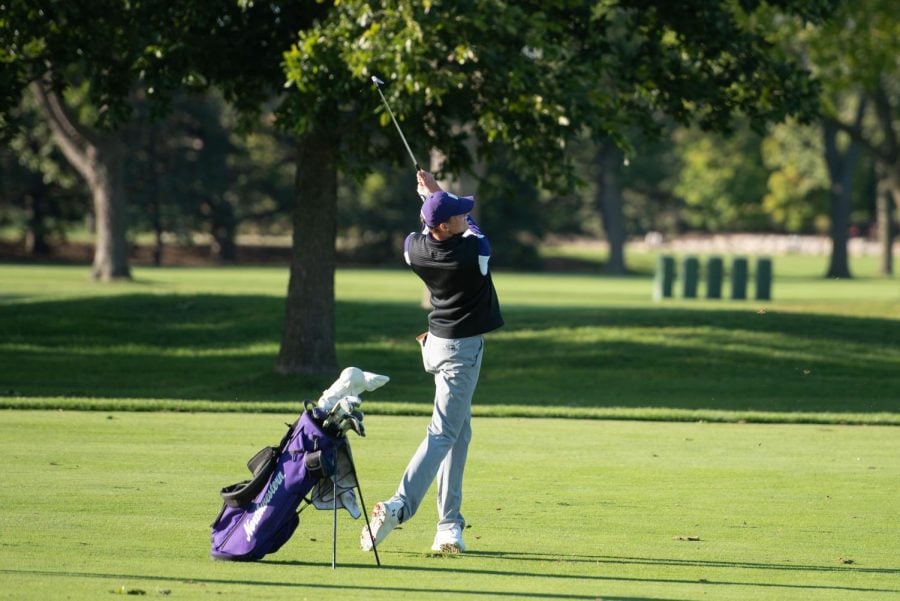 A player in a black vest and purple shirt holds a golf club.