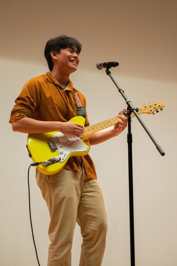 A person plays a yellow electric guitar while singing into a microphone on a stand.