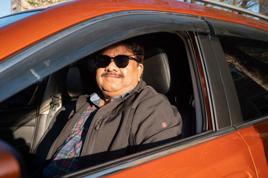A man in black sunglasses poses from inside an orange car.