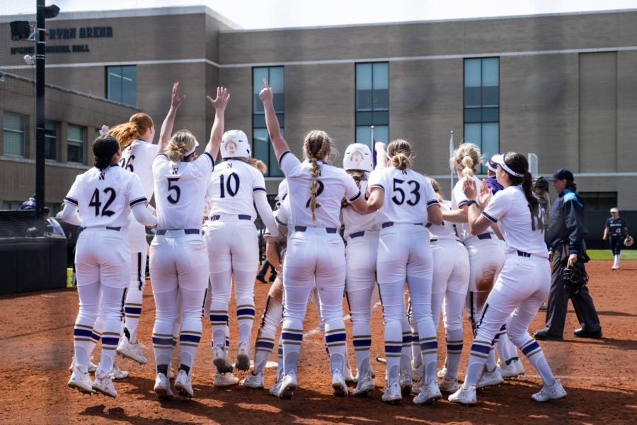 Softball players in purple and white uniforms cheering.