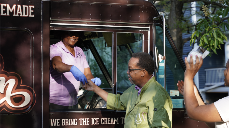 A person is handed ice cream from a vendor in a brown ice cream truck.