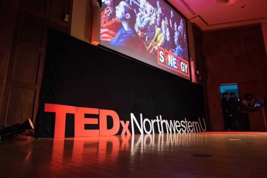 Big letters that read “TEDxNorthwesternU” sit on a red-lit stage.
