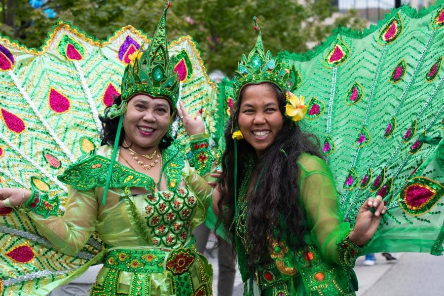 Two dancers wearing green peacock costumes smiles at the camera.